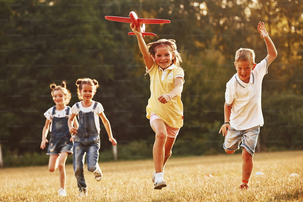 Group of kids having fun outdoors with red toy airplane in hands.