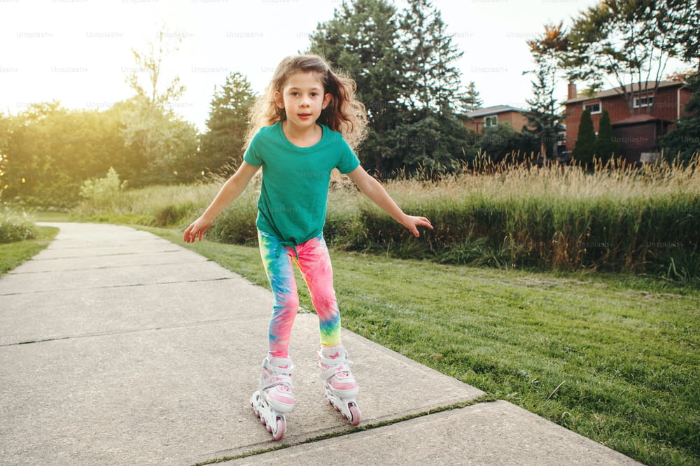 Happy Caucasian girl riding in roller skates on road in park on summer day. Seasonal outdoor children activity sport. Healthy childhood lifestyle. Kids individual summer sport.