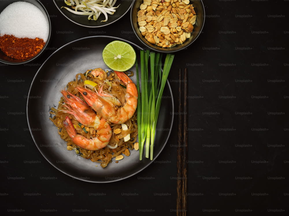 Top view of Pad Thai, stir fried Thai noodle with shrimps on black ceramic plate with lime and chives