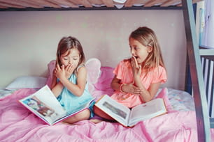 Surprised scared Caucasian sisters girls reading books in bedroom. Home schooling children siblings learned saw unexpected in book. Kids education development learning. Childhood authentic lifestyle.