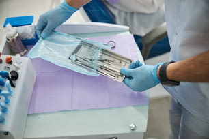 Trabajador médico sacando una bandeja de acero con herramientas estomatológicas en su interior de una bolsa autosellante de polietileno
