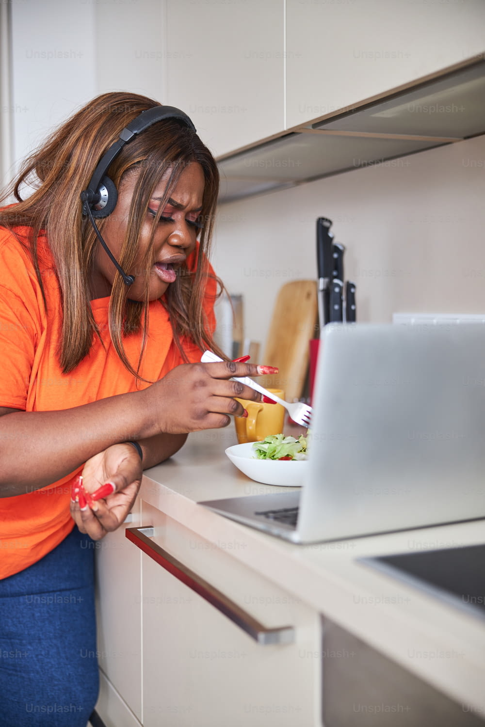 Jeune femme afro-américaine à l’air choqué tout en piquant dans son saladier près d’un ordinateur portable ouvert