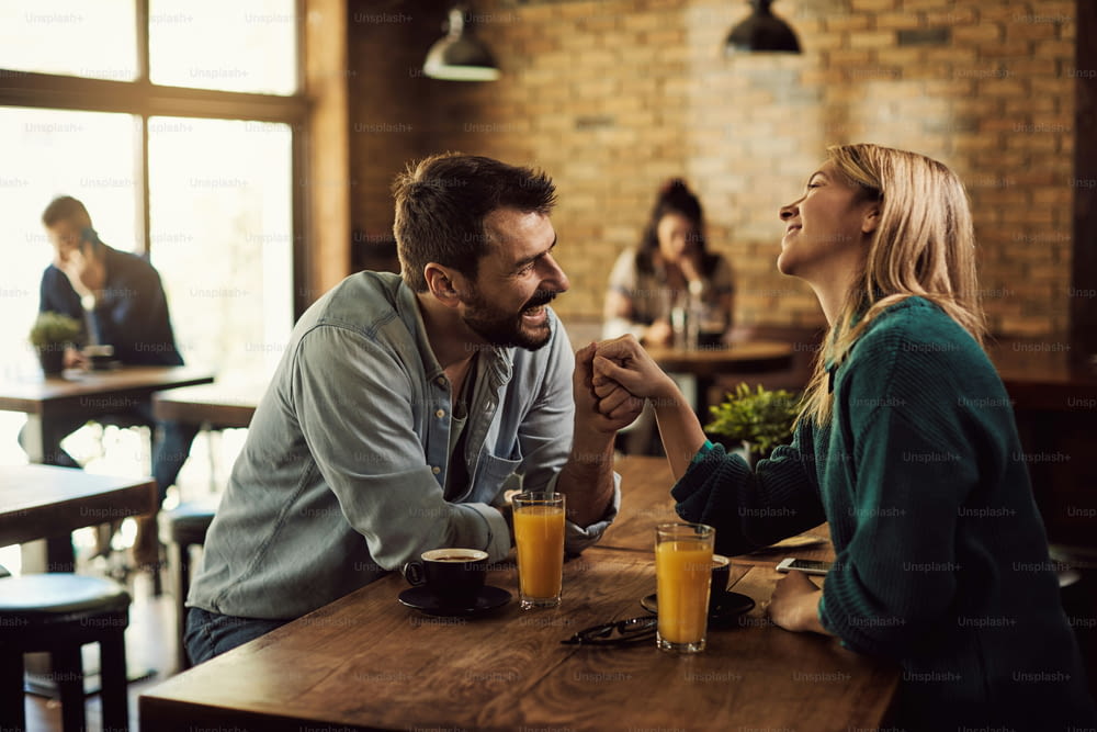 Homme heureux flirtant avec sa petite amie tout en lui tenant la main et en parlant dans un café.