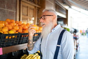 Handsome senior man with beard and eyeglasses choosing organic fruits in the grocery store, buying oranges for fresh juice. Healthy lifestyle, vegan and vegetarian diet concept.
