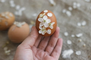 素朴なリネンナプキンに桜の花と花びらで飾られたイースターエッグを手に。春の花が咲く卵の創造的で自然で環境に優しい装飾。ハッピーイースターグリーティングカード