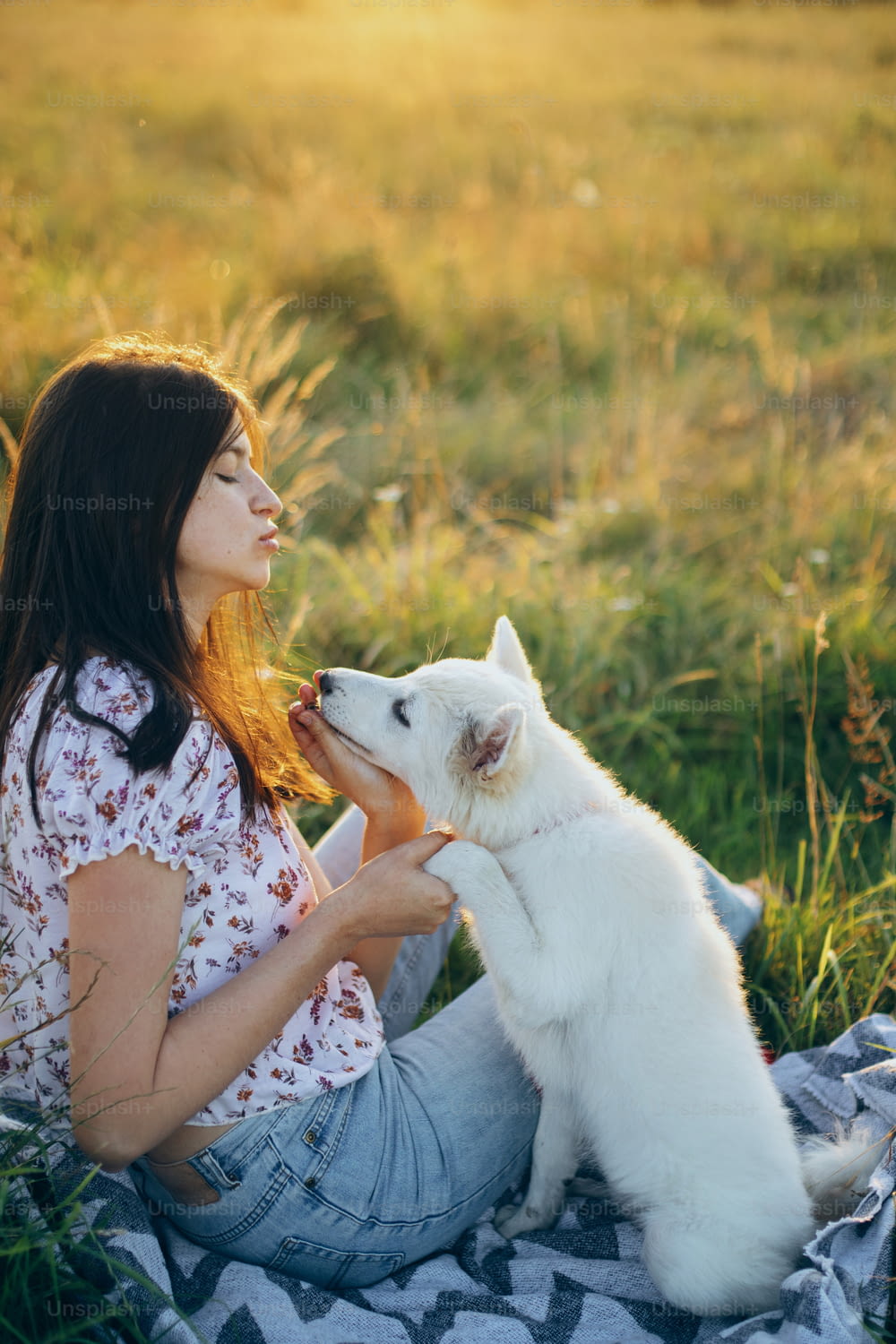 Happy woman training cute white puppy to behave in summer meadow in sunset light. Stylish casual young female relaxing with adorable swiss shepherd fluffy puppy. Vacation with pet