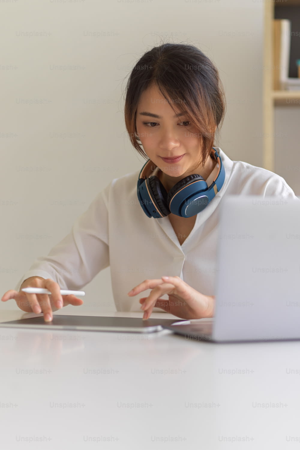 Portrait of a woman with headphone working with laptop and digital table on white desk