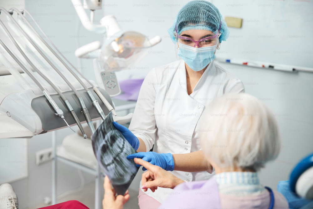 Une professionnelle des soins dentaires partage des informations sur la maladie dentaire d’une patiente en pointant du doigt le film radiographique de ses dents