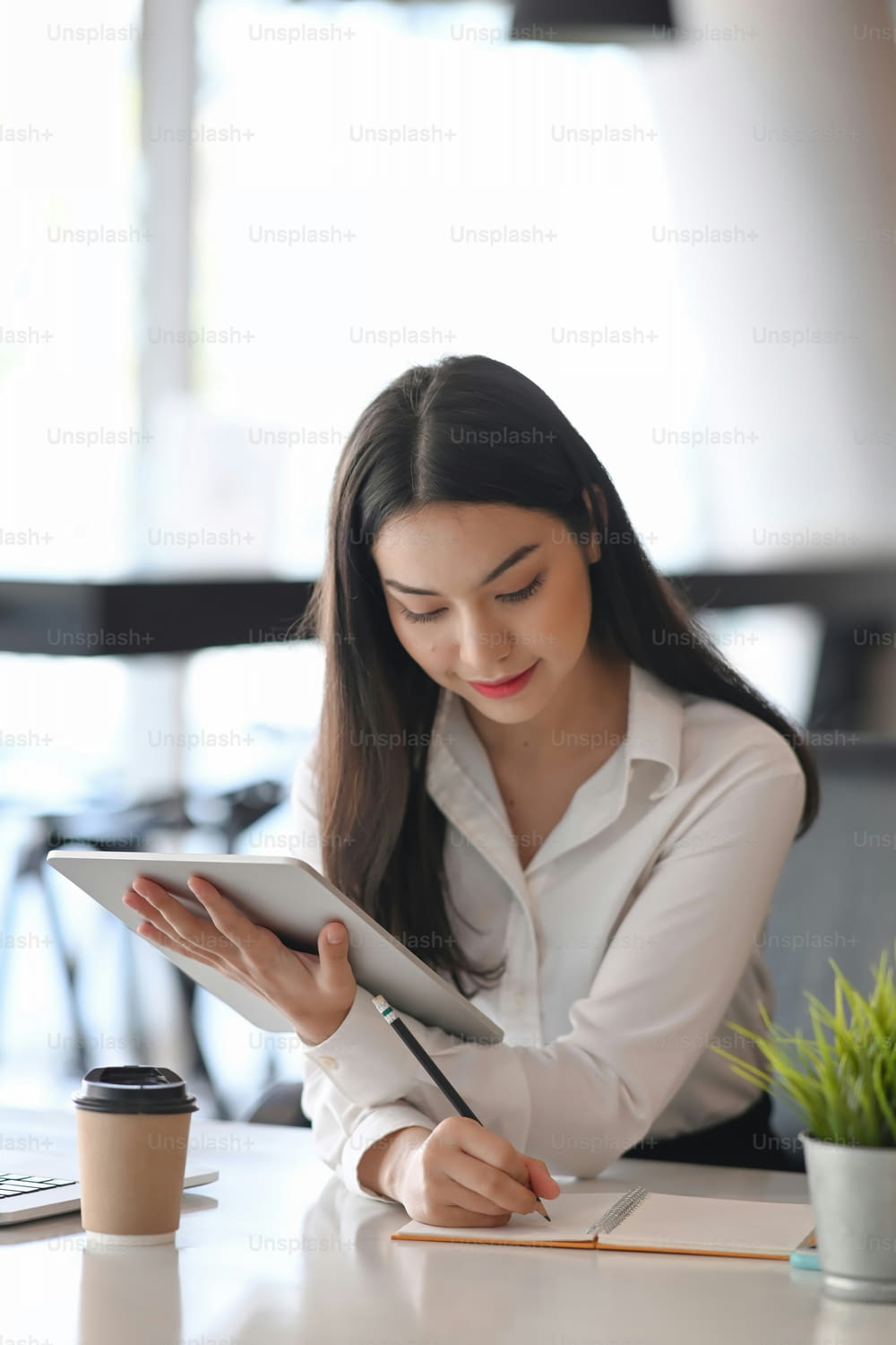 Portrait of young businesswoman using digital tablet and making note on note book.