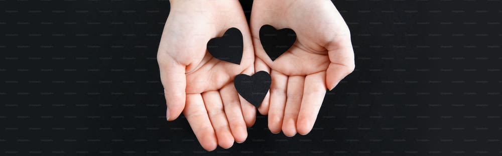 Hands holding black paper hearts on dark background. Support of USA movement protests. People protest against racism. Blackout Tuesday 2020. Banner header for website.