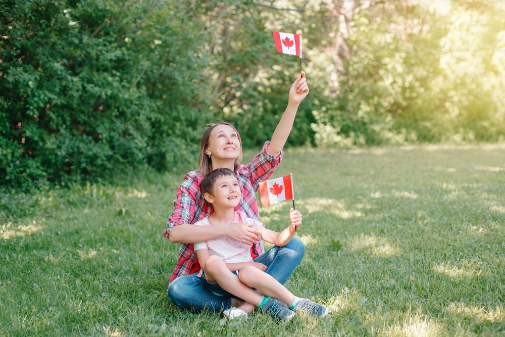 Familienmutter mit Sohn feiert am 1. Juli den nationalen Kanada-Tag. Kaukasische Mutter mit Kind Junge schwenkt kanadische Flaggen. Stolze Bürger feiern den Canada Day im Park im Freien.