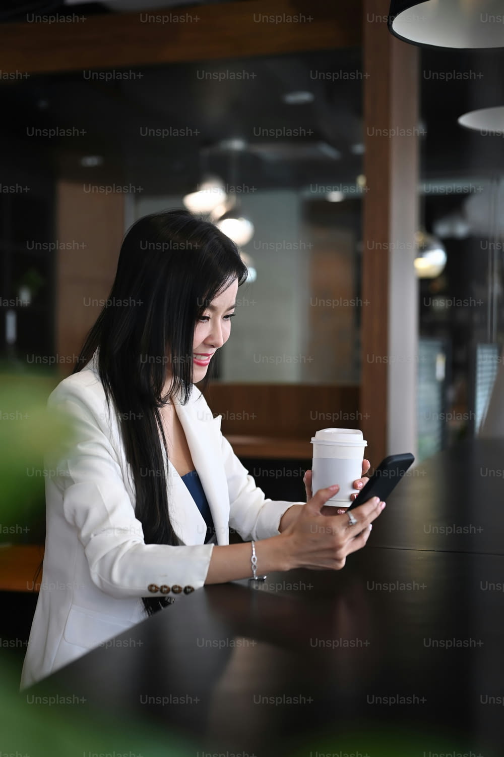 Pleasant woman entrepreneur sitting in modern office shop and using smartphone.