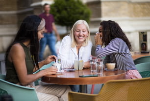 Tres mujeres sentadas en un café en la calle y hablando. La atención se centra en dos mujeres.