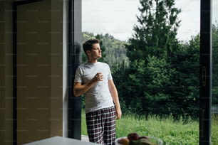 Handsome man enjoying hot coffee in sunny morning on background of mountain hills. Calm tranquil moment. Young man in pajamas relaxing with cup of coffee on porch. Space for text
