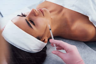 Close up view of woman that lying down in spa salon and have injection by the syringe into her face skin.
