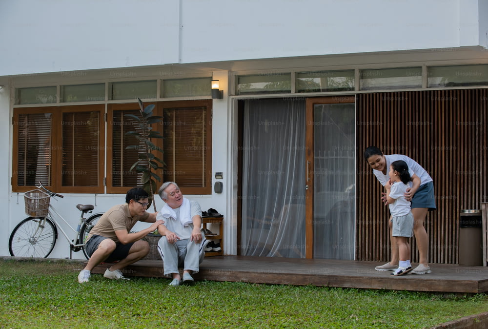 Happy Asian multi-generation family exercising together at home. Father, mother and grandfather with cute baby girl relax and having fun playing and exercising at home front yard in the morning.