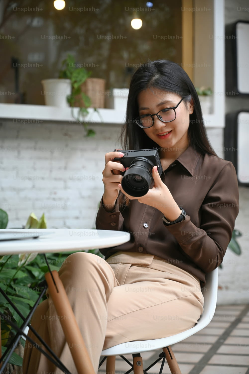 Portrait of smiling young woman sitting in outdoor cafe and checking image on her digial camera.