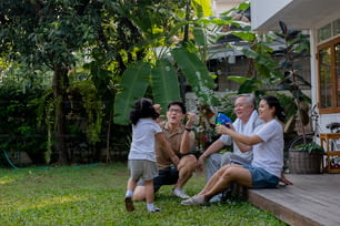 Happy Asian multi-generation family exercising together at home. Father, mother and grandfather with cute baby girl relax and having fun playing and exercising at home front yard in the morning.