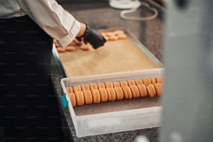 Foto ritagliata di un cuoco professionista che ordina e confeziona innumerevoli macarons color pesca in contenitori