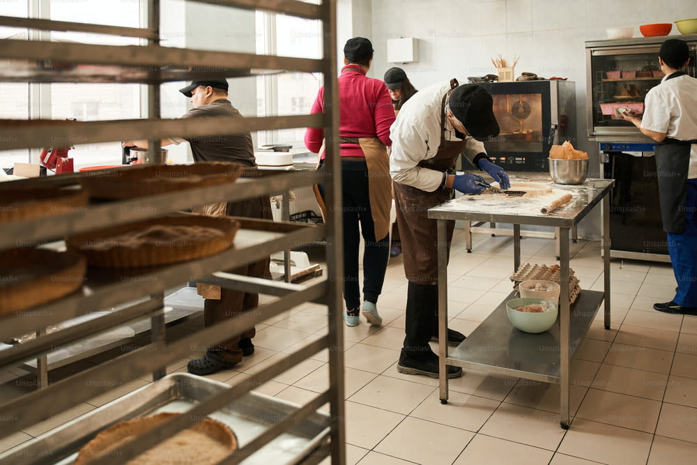 Proceso de cocción. Vista de cuerpo entero de la cocina con los trabajadores preparando una sabrosa panadería para el salling. Todo el mundo está ocupado con su propio proceso. Foto de archivo