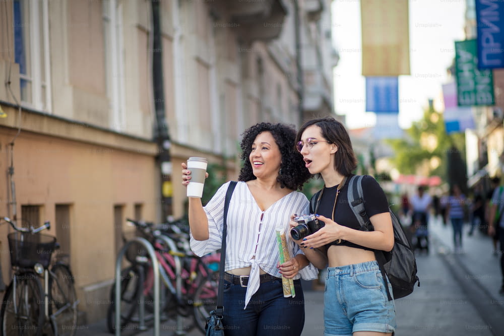커피 한 잔과 카메라를 손에 들고 거리에 서 있는 웃는 여자들.