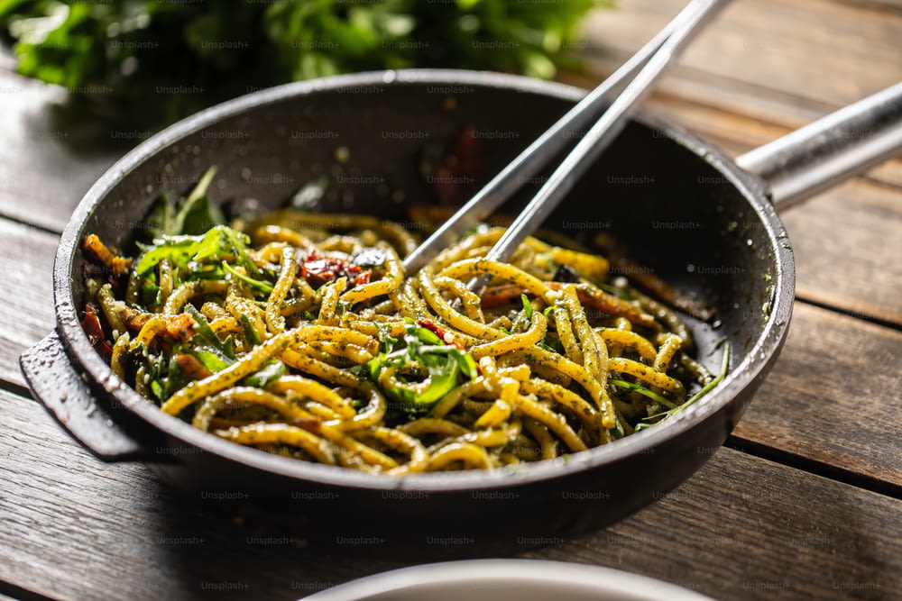 Spaghetti au pesto et au parmesan dans une poêle foncée avec une pince à épiler.