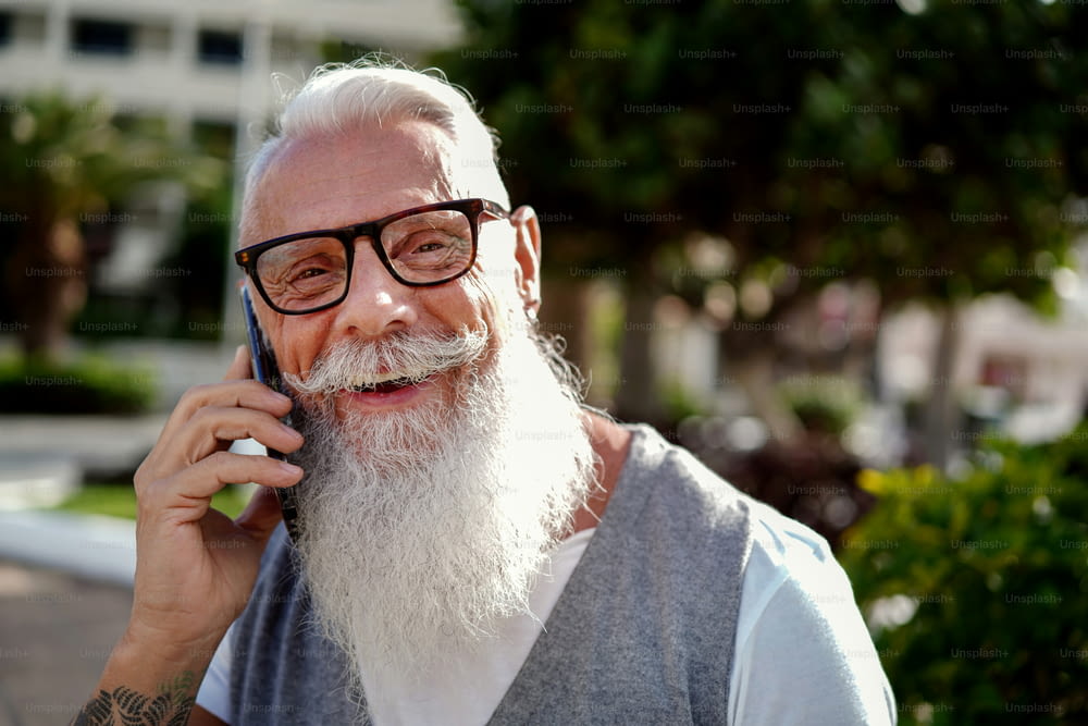 Close up photo of handsome senior man with mustache and beard talking on mobile phone, smiling and looking to the camera . Authentic Senior Retired Life Concept.