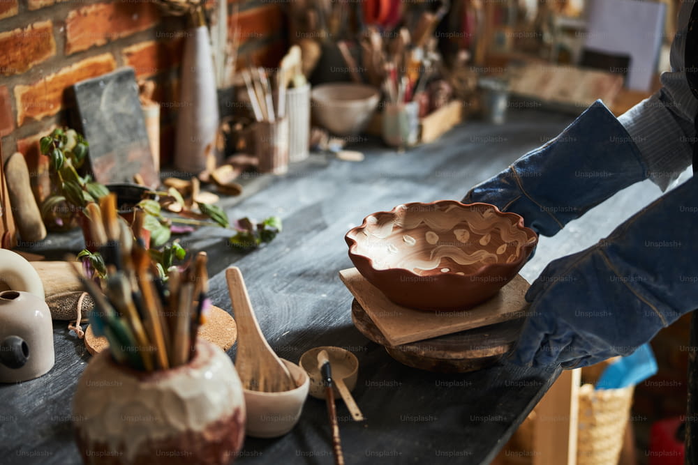 美術陶芸工房で作業しながら陶器の鉢を持つ手袋をはめた陶芸家の接写