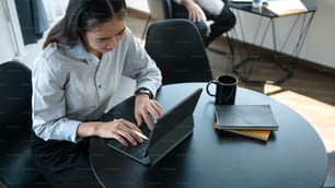 Smiling young asian woman employee sitting in office room and using computer tablet.