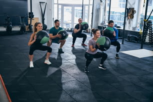 Groupe de cinq sportifs qui s’entraînent ensemble avec des ballons de stabilité dans une salle de fitness