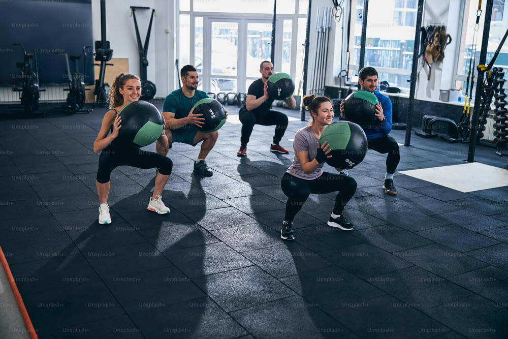 Group of five sporty people working out together with stability balls in a fitness studio