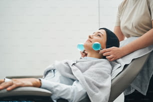 Heureux serein jeune client de salon de beauté attrayant allongé dans le fauteuil pendant la procédure de raffermissement de la peau