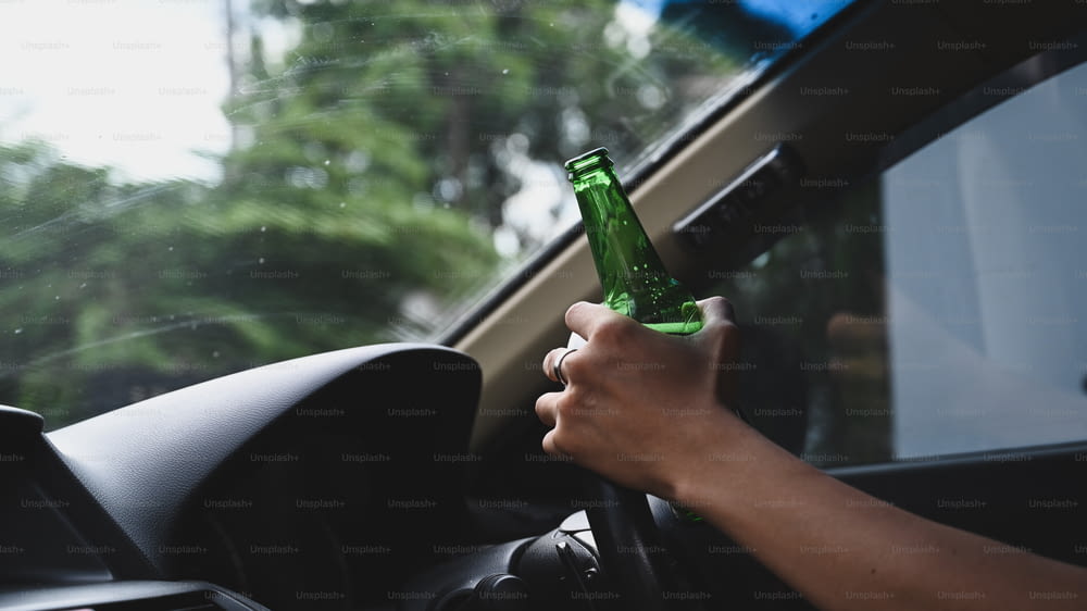 차를 운전하는 남자는 맥주 한 병을 들고 있습니다. 술을 마시고 개념을 운전하지 마십시오.