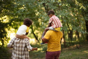 Afroamerikanische Familie, die durch den Park geht. Eltern, die Kinder huckepack tragen.