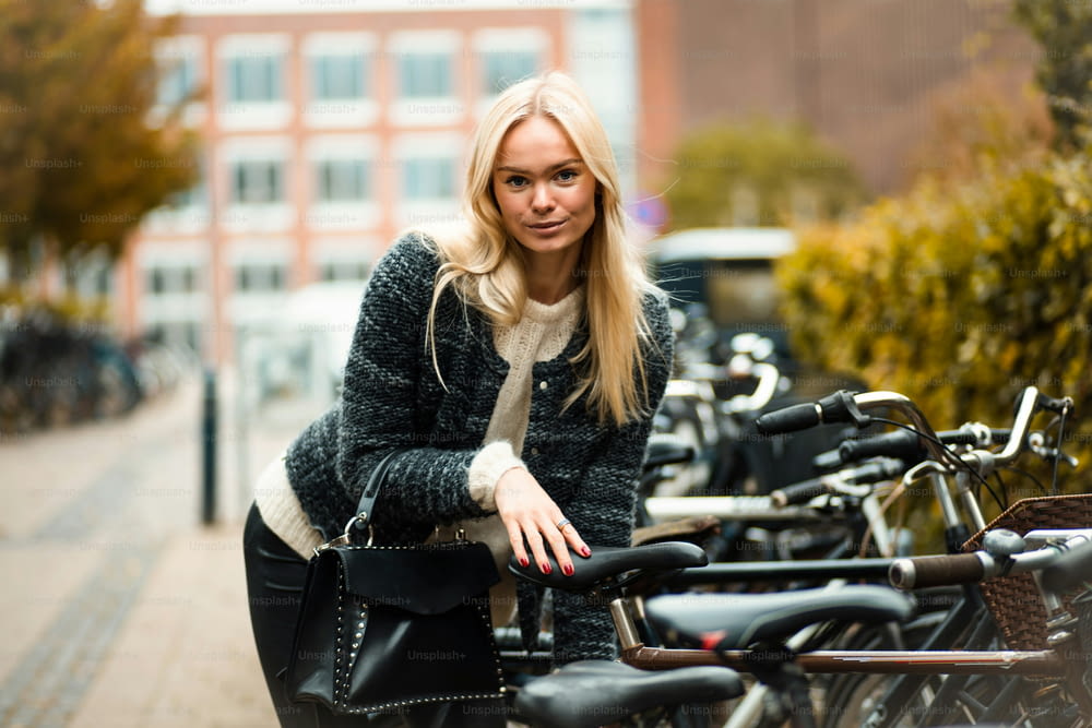 Blond woman standing on street by the bicycle. Focus is on woman.