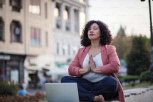 African American businesswoman sitting in lotus pose. Business woman working yoga on the street.