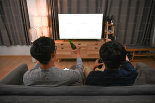 ソファに座りながらビールを飲みながらテレビを見ている2人のアジア人男性。