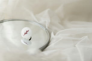 Elegante anello rotondo bianco moderno su specchio su morbido tulle bianco, spazio di copia. Insolito anello in vetro fuso alla moda. Regalo contemporaneo