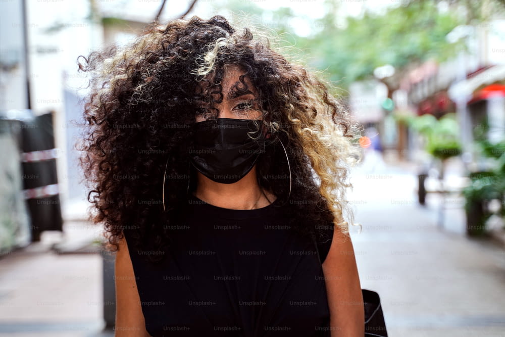 Afro Woman walking on the city street wearing surgical mask against disease coronavirus. Girl with face mask respecting social distancing during Pandemic.