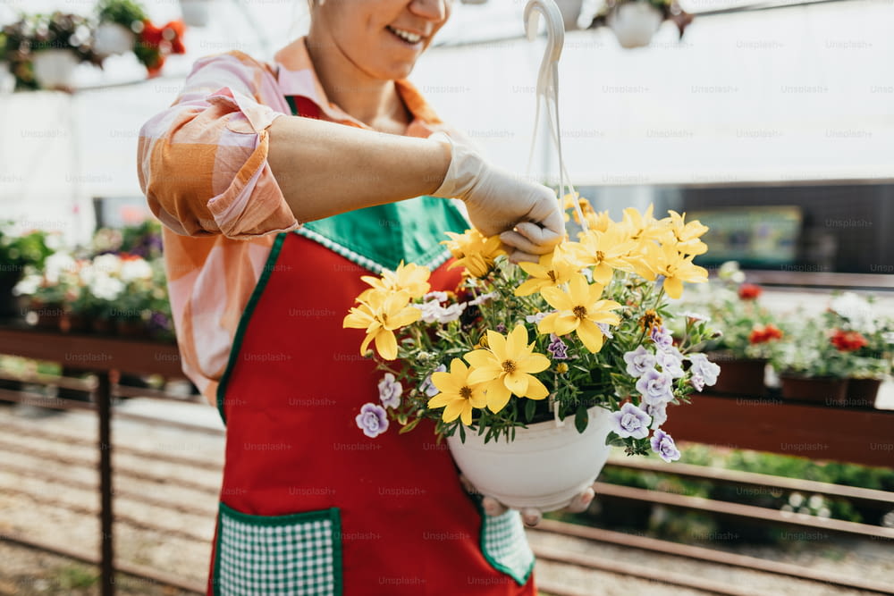 행복하고 긍정적인 젊은 성인 여성은 온실에서 일하고 아름다운 꽃을 즐기고 있습니다.