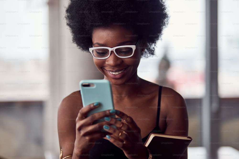 Cheerful african american woman holding smartphone and notepad.
