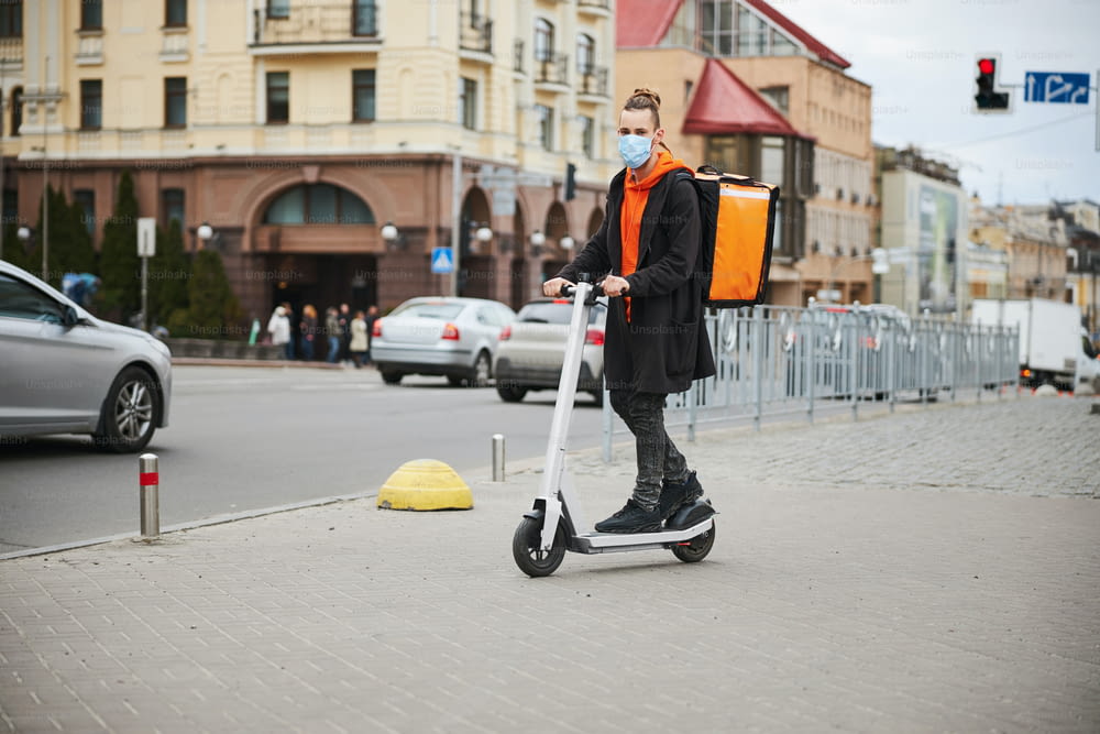 Corriere allegro che indossa uno zaino termico mentre consegna cibo in scooter