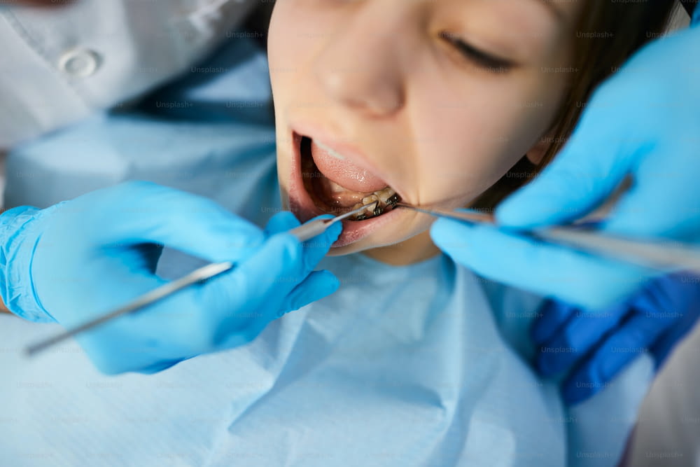 Close-up of teenage girl getting her teeth examined by dentist at dental clinic.