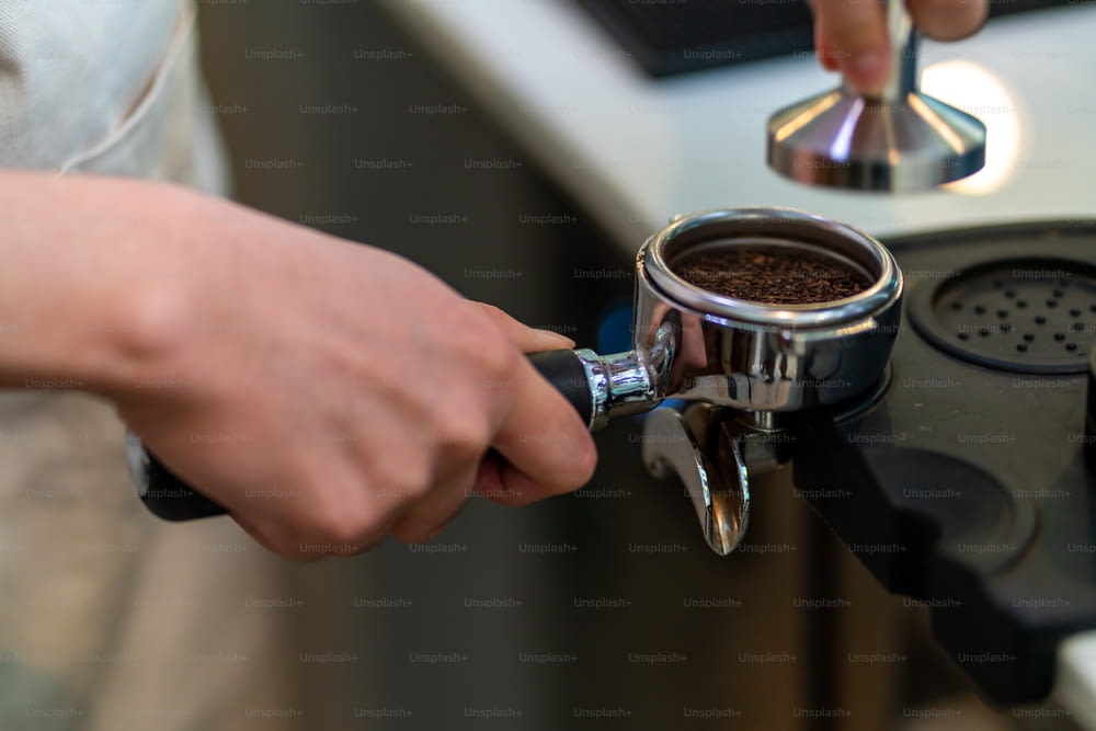 Empleado a tiempo parcial de la cafetería del hombre asiático prepara café caliente en una máquina de café. Barista masculino que hace espresso con café molido en cafetera. Propietario de una pequeña empresa y concepto de trabajo a tiempo parcial.