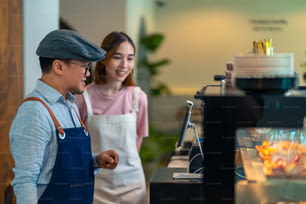 Asian male coffee shop manager teaching young woman staff working on digital tablet. Small business cafe and restaurant owner instruct part time employee preparing service to customers before opening
