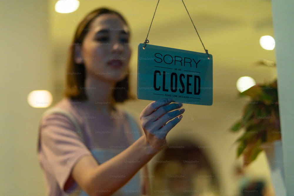 Femme asiatique barista de café marchant vers la porte du café et tournant suspendu signe fermé. Serveuse préparant le restaurant pour le service au client. Propriétaire d’une petite entreprise et concept de travail à temps partiel