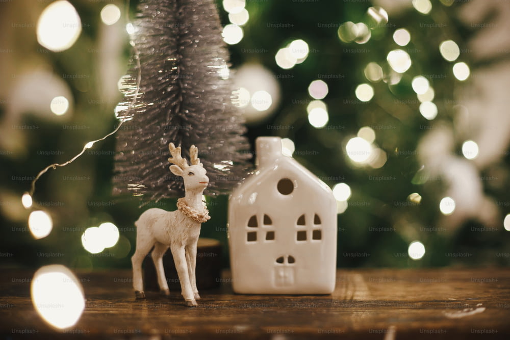 Elegante árbol de navidad, juguete de reno y casa en madera rústica sobre fondo de luces navideñas. Hermosa escena navideña. Feliz Navidad. Mágica época navideña. Espacio para el texto