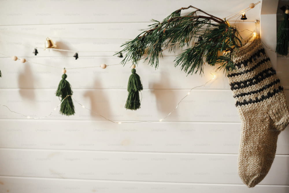 Bas rustique de Noël avec branche de sapin et guirlande élégante avec des cloches et des arbres sur un mur en bois blanc avec des lumières de Noël. Chambre scandinave décorée de manière festive. Décor moderne fait à la main