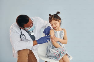Jovem médico afro-americano dando injeção a menina no hospital.