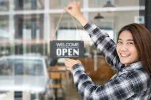 Small business owner turning open sign board on glass window.